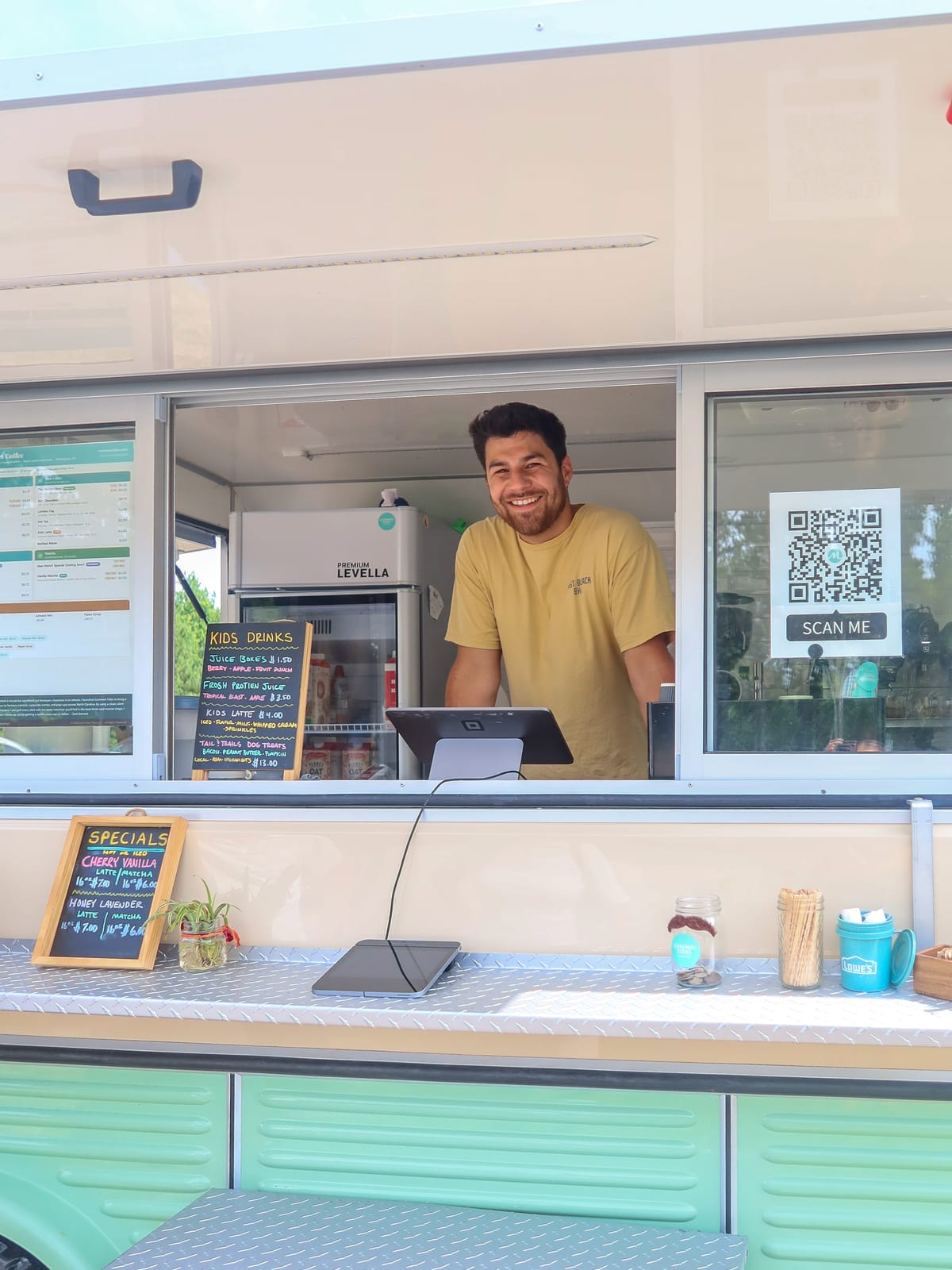 Zack Bennett, founder of Common Tides Coffee, smiling from the window of his vintage mobile espresso trailer in Wilmington NC